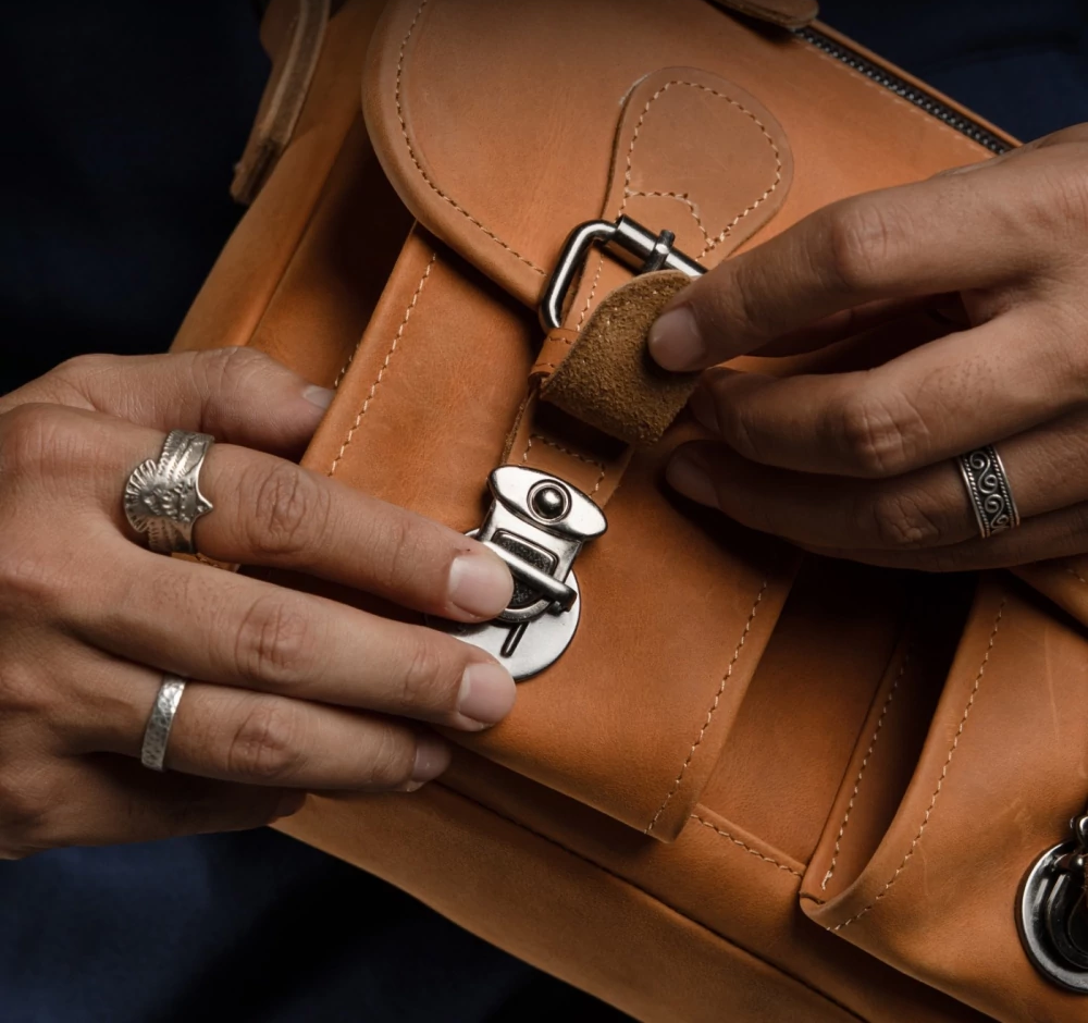 Hands fastening buckle closure on brown leather messenger bag.